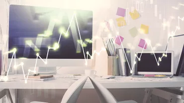 Office with computers displaying graphs, white desks, and colorful sticky notes.