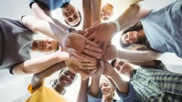 Group of people stacking hands in a circle, viewed from below.