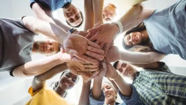 Group of people stacking hands in a circle, viewed from below.