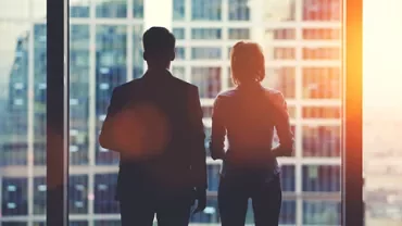 Silhouettes of two people looking out a window at a cityscape.