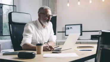 Person working at a desk with a laptop and papers in a modern office setting.