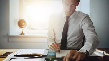 Person working at a desk with documents and a calculator in sunlight.