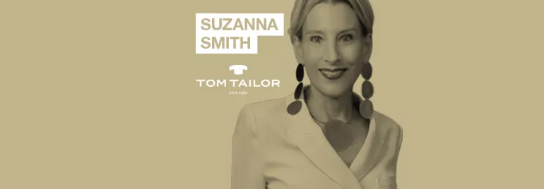 Person smiling, wearing a white blazer and large earrings, with text 'SUZANNA SMITH' and 'TOM TAILOR'.