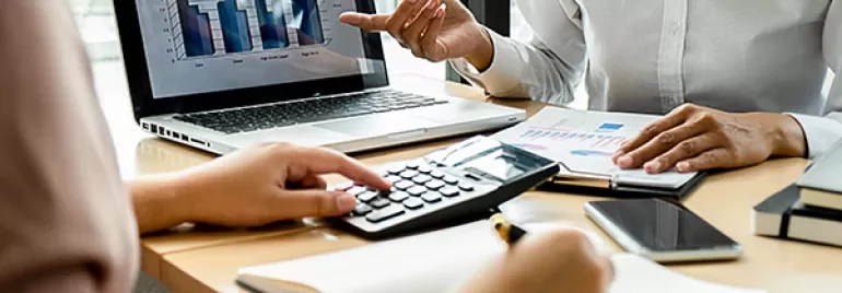 Two people discussing charts and notes at a desk with a laptop.