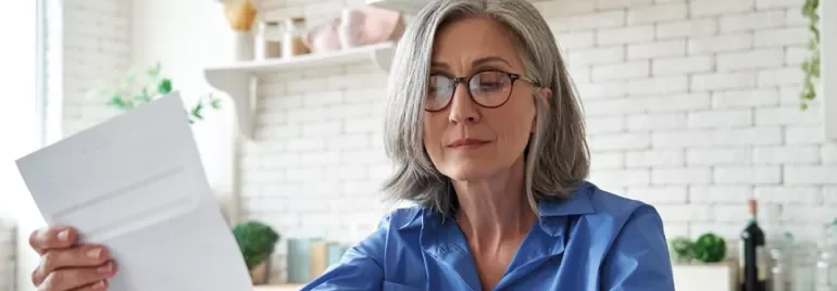 Person in blue shirt reading a document in a bright kitchen.