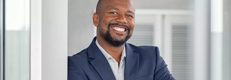 Person smiling in a suit, leaning against a pillar.