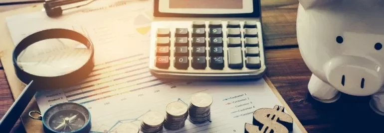 Calculator, coins, magnifying glass, and piggy bank on financial documents.