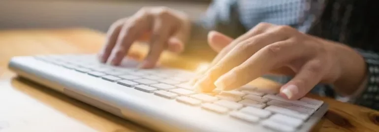 Close-up of hands typing on a white keyboard.