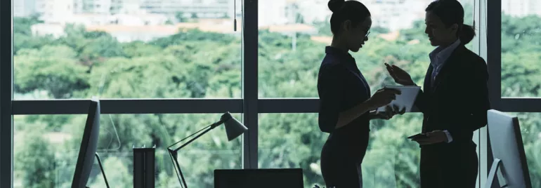Two individuals discussing in an office with a window view of the city.