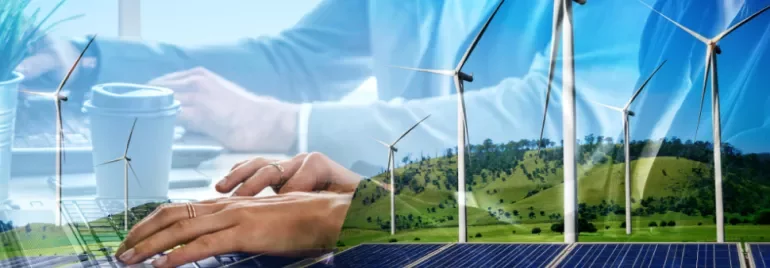 Hands typing on a laptop with wind turbines and solar panels in the background.