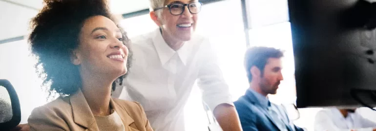 Colleagues collaborating at a computer in a bright office.