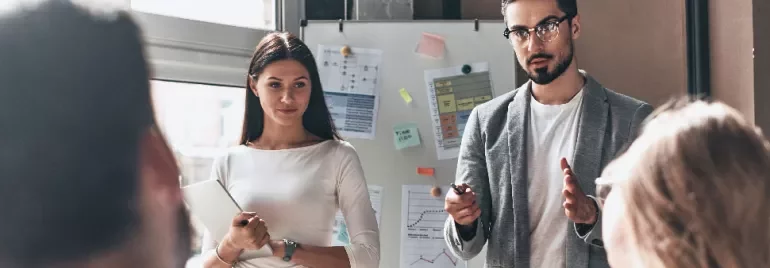 Two people presenting data on a whiteboard during a meeting.