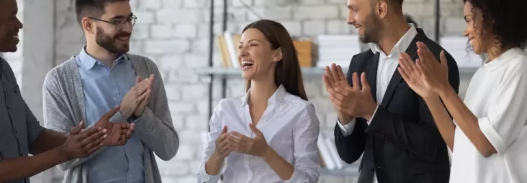 Group of colleagues in an office, smiling and clapping.