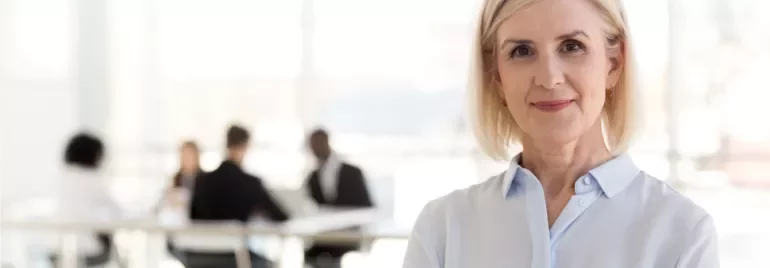 Person smiling in office setting, with colleagues in the background.
