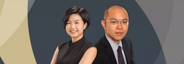 Two professionals smiling in formal attire against a geometric background.