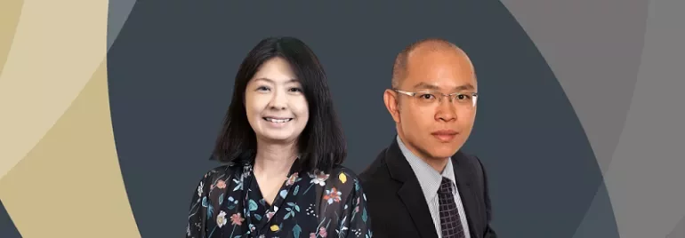 Two people smiling, one in a floral blouse and the other in a suit, against a geometric background.
