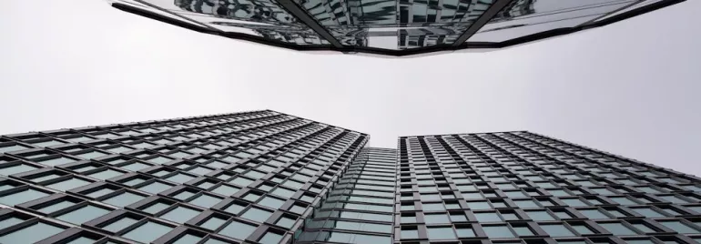 Upward view of mirrored glass skyscrapers against a cloudy sky.