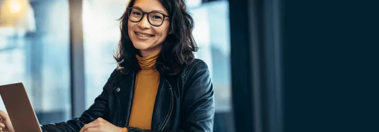 Person with glasses smiling and using a laptop indoors.
