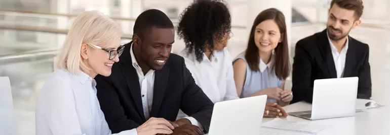 A diverse group of professionals working together on laptops at a bright, modern office table.