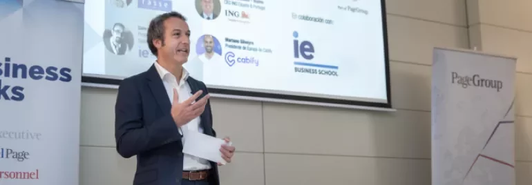 a man talking in a conference with a screen in the background