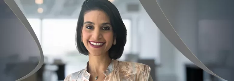 Person in patterned blouse standing in a modern office setting with curved graphic elements.