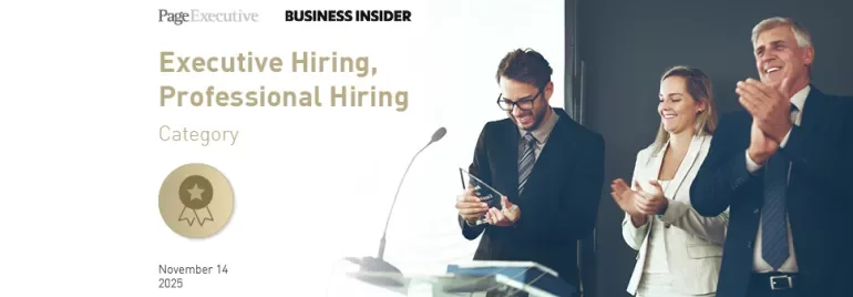 People standing on a stage during an award presentation, with one person holding a trophy while others applaud.