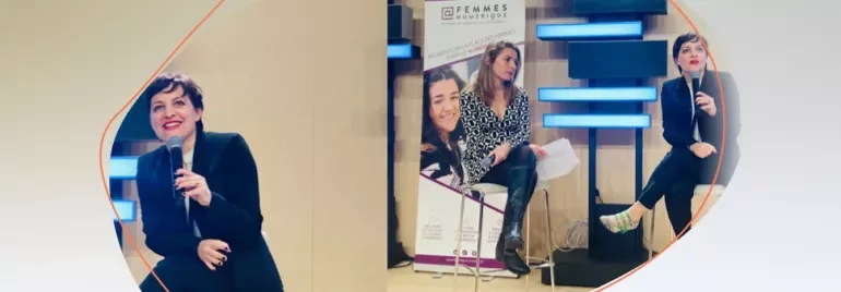 Three individuals seated on a stage during a discussion, with microphones and a banner displayed in the background.