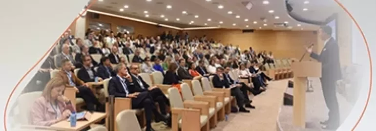 Large audience seated in an auditorium while a speaker presents at a podium.