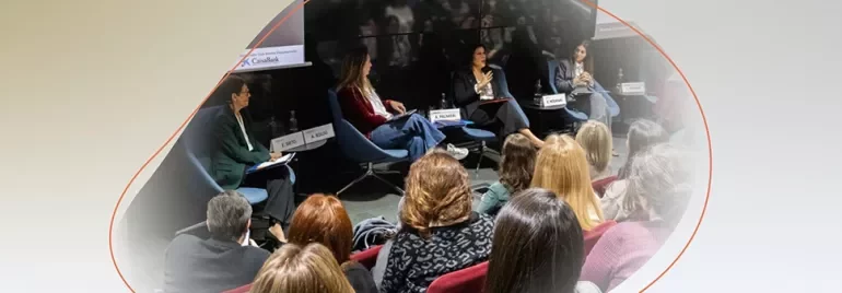 Panel discussion with several people seated on stage, speaking to an audience in a conference room.