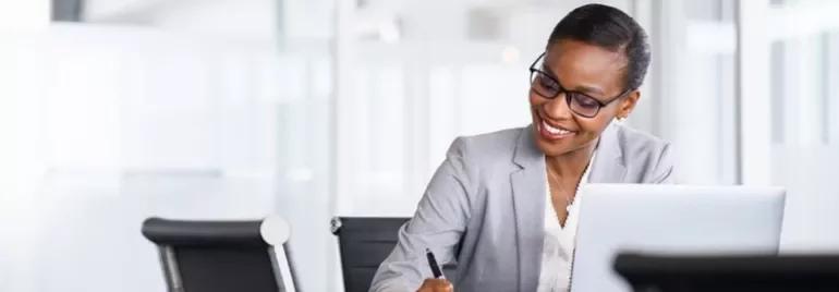 Professional working on a laptop and taking notes in an office setting.