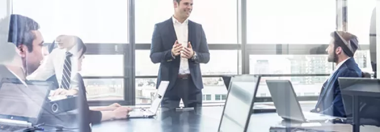 Person leading a business meeting in a modern office with several people seated around a table.