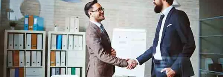 Two people shaking hands in a modern office setting.