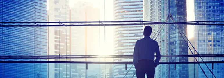 Person looking out at city skyline through large office window.