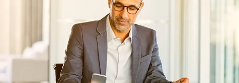 Person in a suit looking at their phone while sitting at a desk.