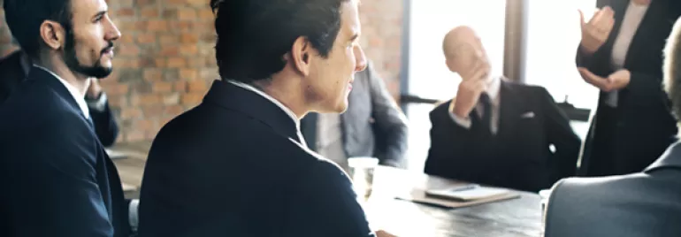 People in a meeting room with a brick wall and sunlight streaming through windows.