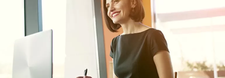 Person smiling while working on a laptop near a window.