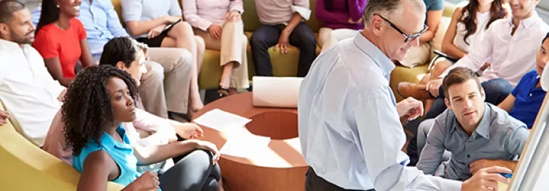 A group of people in a relaxed meeting setting with a speaker at the front.