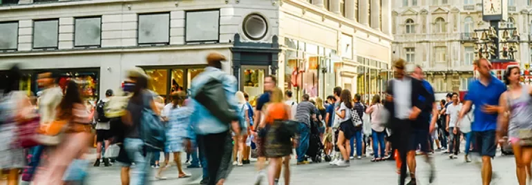 A bustling city street with people walking past shops.