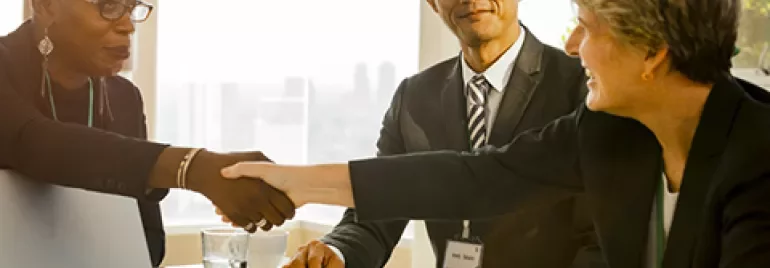Three people in a meeting room, two shaking hands and smiling.