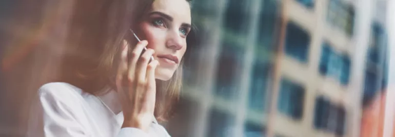Person looking thoughtful while talking on a phone, standing by a window.