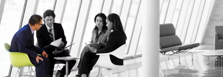 Group of four people seated in a modern office, engaged in discussion.
