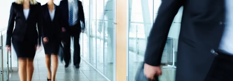 People in business attire walking in a modern office hallway.