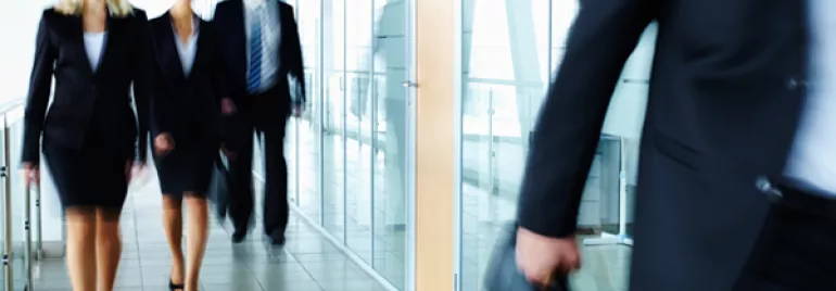 People in business attire walking in a modern office hallway.