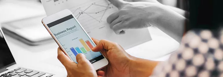 Person holding a smartphone displaying a business report with colorful charts.