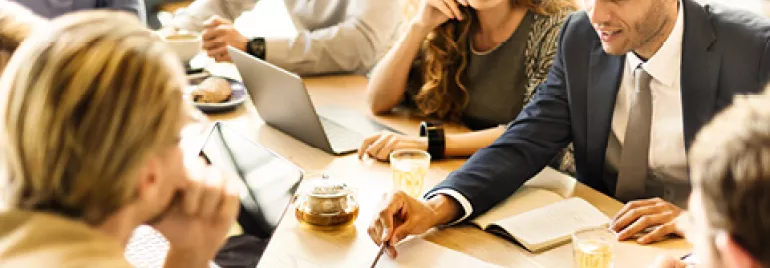 Group of people discussing in a meeting with laptops and notebooks on a table.