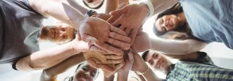 Group of people stacking hands in a circle, viewed from below.