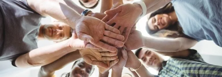 Group of people stacking hands in a circle, viewed from below.