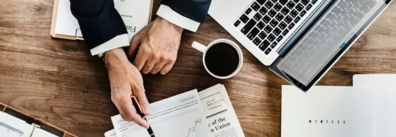 Person reviewing financial charts at a wooden desk with laptop and coffee.