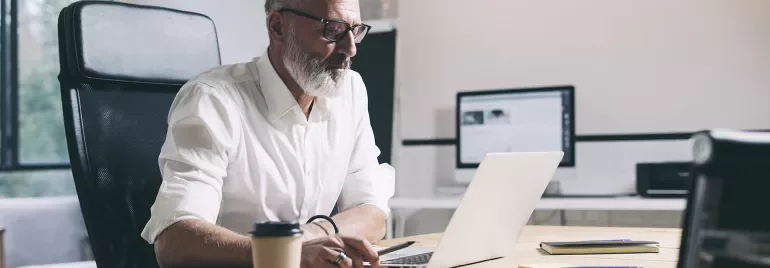 Person working at a desk with a laptop and papers in a modern office setting.