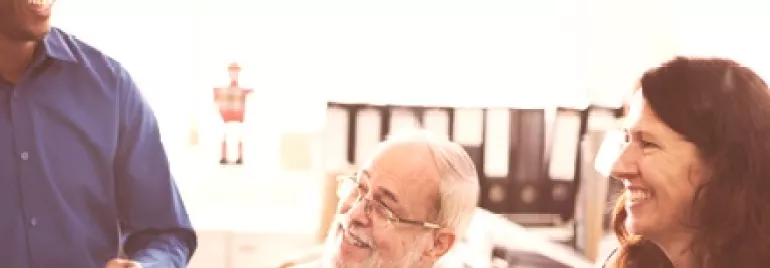 Three people smiling and discussing in an office setting.
